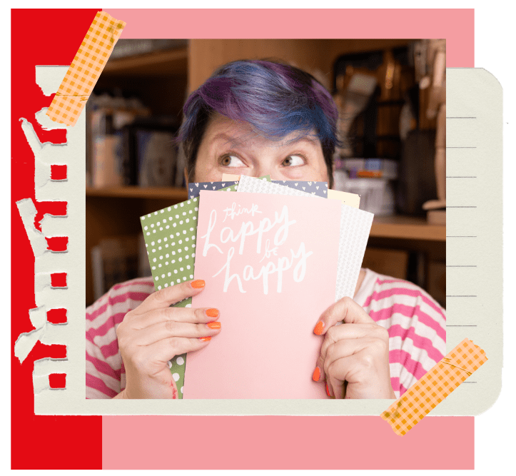 Maria Pascoal with blue and purple hair holding "Think Happy, Be Happy" cards in a creative scrapbook frame.